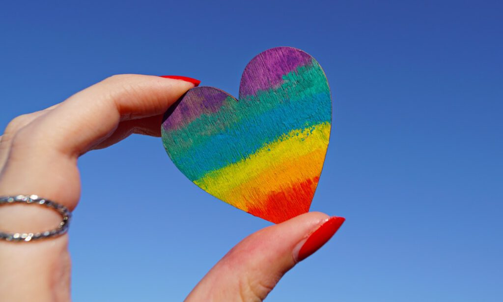 Hand is holding heart colored as rainbow